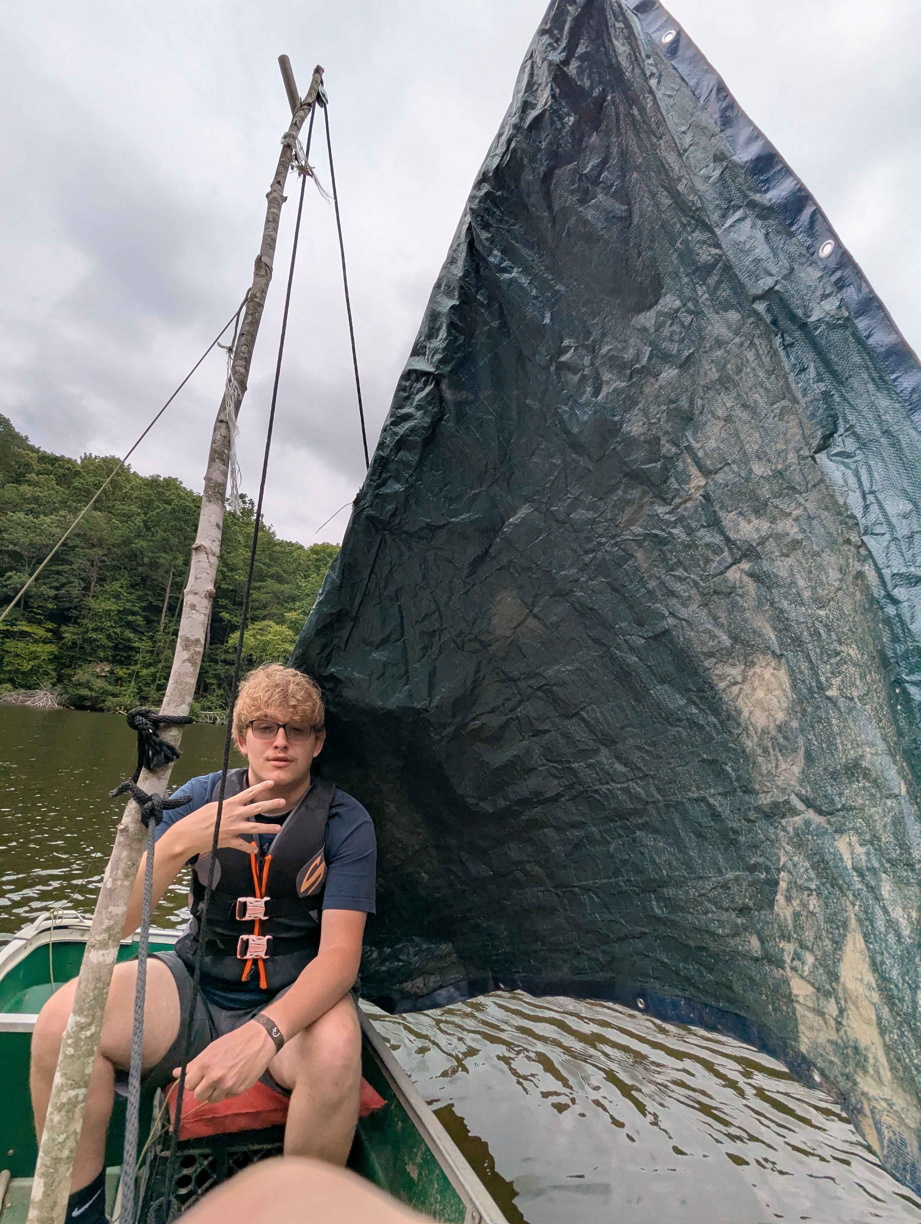 A fellow sitting in the previously pictured sailboat, making a stupid hand signal.